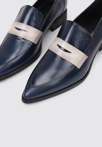 Zapatos de cuero azul marino con punta afilada y una correa beige en la parte superior, con un detalle troquelado. Suela duradera, con un tacón ligeramente elevado.