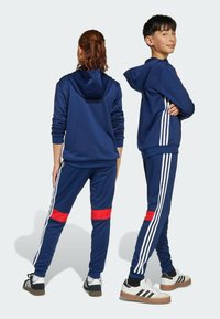 Navyblauer Hoodie und Hosen-Set, das weiße Streifen und einen roten Akzent an den Hosen aufweist. Hergestellt aus glattem Stoff mit lässigem Schnitt.