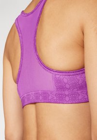 Sujetador deportivo morado con un diseño de espalda nadadora. Presenta un acento de encaje texturizado a lo largo de la banda inferior. Tejido suave y elástico.
