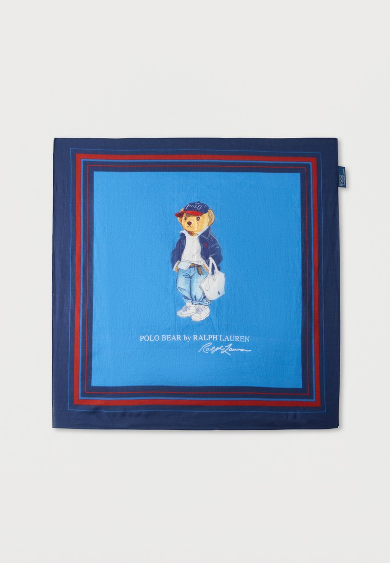 Μπλε κασκόλ με κόκκινο και ναυτικό περίγραμμα που απεικονίζει μια αρκούδα που φοράει καπέλο, μπουφάν, τζιν, αθλητικά παπούτσια και κρατά μια λευκή τσάντα tote.