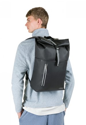 Sac à dos noir à rabat roulé fabriqué en matériau imperméable, doté d'une poche avant zippée et de bretelles ajustables. Design minimaliste et finition mate.