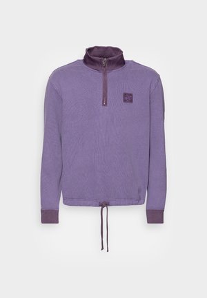 Pull violet à manches longues avec zip quart, poignets côtelés, ourlet ajustable avec cordon de serrage et petit logo patch poitrine sur fond uni.