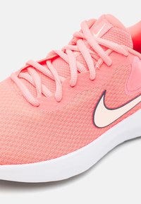 Chaussure de sport en mesh rose avec une tige texturée, un logo Nike swoosh beige contrastant et une semelle en caoutchouc blanche. Caractéristiques : lacets plats et col rembourré.