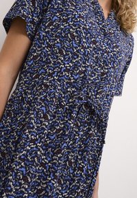 Rochie cu imprimeu floral în navy, cu modele albastre, albe și roșii. Mâneci scurte, închidere cu nasturi în față și detaliu cu talie legată. Material ușor.
