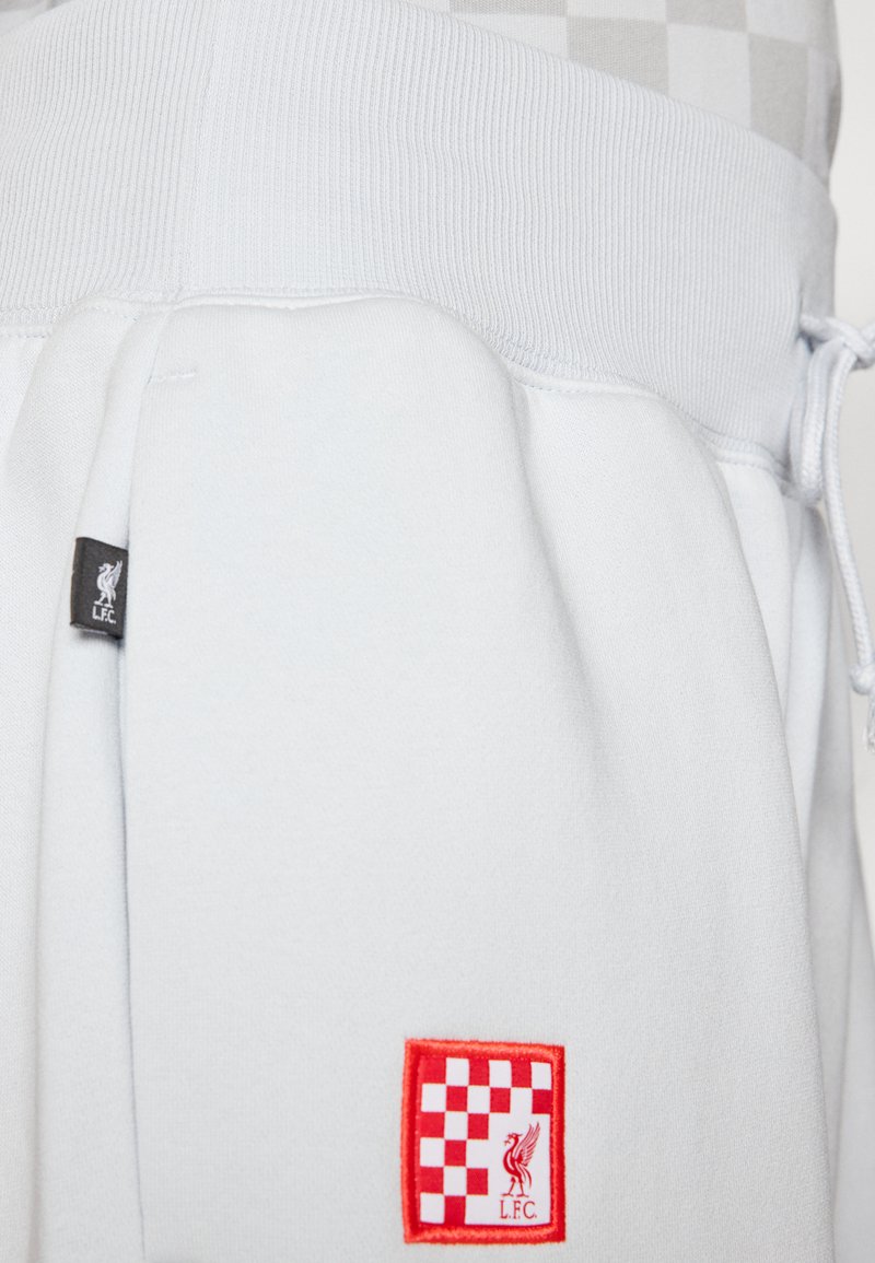 Pantaloni jogging azzurri con vita a costine, dotati di una toppa quadrata rossa con motivo a scacchi e il logo del Liverpool Football Club.