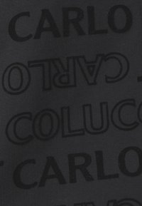 Juodas audinys, turintis iškilias raides su pakartotiniais pavadinimais "CARLO" ir "COLUCCIO" kontrastinga juoda spalva.