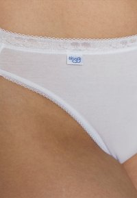 Białe bawełniane stringi z delikatną koronką, z małą niebieską metką Sloggi na pasku, gładka struktura i minimalistyczny design.