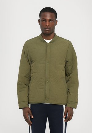 Olive green quilted bomber jacket with a round neckline, front snap buttons, and subtle textured pattern. Model wears a white shirt underneath.