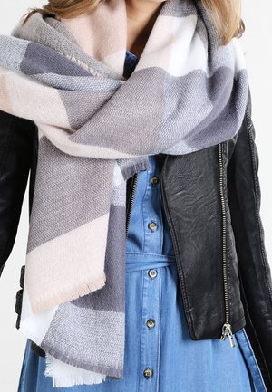 Grand foulard doux aux teintes pastel atténuées enroulé autour du cou, porté sur une veste en cuir noire et une robe bleue boutonnée.