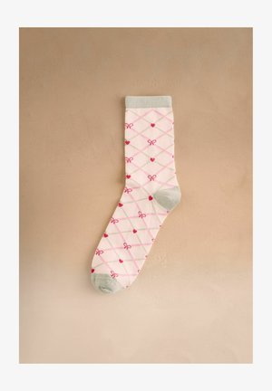 Valge sokk halli varba ja mansetiga, kaunistatud roosa ja beeži ruudustikuga, punaste südamete ning väikeste punaste lipsukestega beežil taustal.