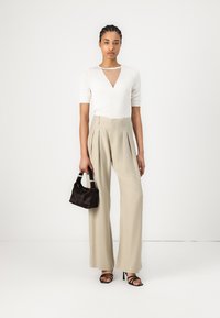 Bijela kratka majica s kratkim rukavima, V-izrezom i detaljem izrezivanja, u kombinaciji s bež širokim hlačama i crnom torbicom s teksturom. Crne sandale s trakama.