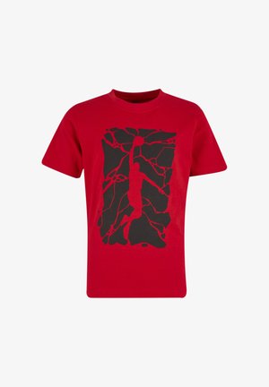 T-shirt rouge à manches courtes avec un motif noir représentant un joueur de basket sautant et attrapant un ballon au milieu de formes fissurées.