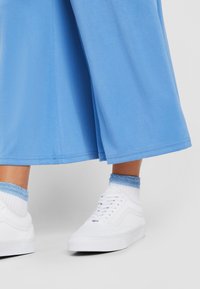 Light blue wide-leg pants, cotton fabric, with a smooth texture, paired with white sneakers and blue-accented socks.