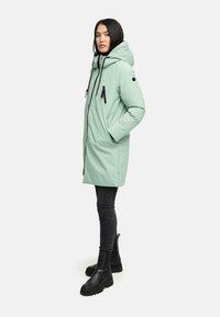 Mintgrøn parka med hætte, lynlåslommer og sorte detaljer. Bæres over mørke skinny jeans og kraftige sorte støvler. Glat tekstur.