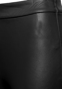 Czarne spodnie z eko skóry o gładkiej fakturze. Posiadają wysoki pas i boczny zamek błyskawiczny do zamknięcia. Cienkie pionowe przeszycia jako detal.