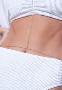 Valkoinen teksturoitu bikinitoppi, joka on yhdistetty herkän kultaketjun kanssa korostamaan vyötäröä, jossa on pieniä pyöreitä ja pitkänomaisia linkkejä.
