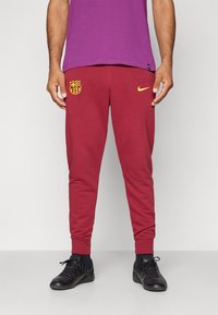 Bordo sporta bikses ar zelta Nike logotipu un FC Barcelona emblemu. Piedāvā slaidu piegriezi un ribotas aproces drošai izskatam.