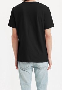 Camiseta de algodón negra con escote redondo, mangas cortas y un corte relajado, combinada con unos vaqueros de un azul claro descolorido. Sin gráficos visibles.