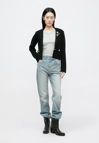 Μαύρο εφαρμοστό σακάκι με χρυσά κουμπιά, γκρι μπλούζα, ξεβαμμένο μπλε τζιν και μαύρα μποτάκια αστραγάλου. Λείο ύφασμα και δομημένες σχεδιαστικές λεπτομέρειες.