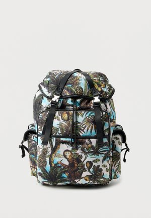 Sac à dos avec des bretelles noires présentant un imprimé tropical coloré avec des singes, des ananas et des palmiers sur un fond clair.