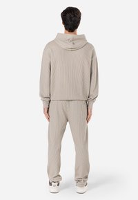 Hanorac bej deschis cu cusături pe spate, textură ribbed și manșete elastice, purtat cu pantaloni asortați ribbed și adidași albi.