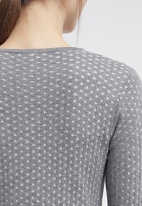 Grau gestrickter Pullover mit einem strukturierten Muster aus erhabenen weißen Punkten. Rundhalsausschnitt und lange Ärmel, mit einer glatten, weichen Oberfläche.