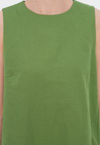 Grünes ärmelloses Oberteil aus strukturiertem Stoff, mit hohem Ausschnitt und subtilen seitlichen Nähten, in schlichtem Design.