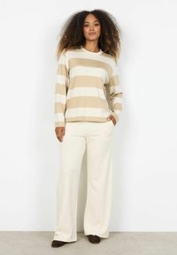 Beige en wit gestreepte trui met lange mouwen en een ronde hals, gecombineerd met crème wijde broekspijpen en donkere schoenen. Gladde stof; losse pasvorm.