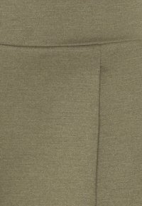 Posnetek v bližini tkanine olivno zelene barve z nežno vodoravno rebrasto teksturo ter šivom, ki poteka navpično in vodoravno.