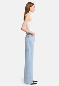 Jeans larges bleu clair avec une taille haute, en denim, deux poches latérales et des détails de couture minimales, associés à un débardeur blanc ajusté.