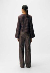 Geknipte, donkere geblokte top met klokmouwen, gecombineerd met hoog aangebrachte, wijd uitlopende brown trousers. Gladde stoffen, minimale details.