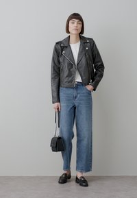 Black leather biker jacket with silver hardware, white shirt, high-waisted blue jeans, black loafers, holding a small black purse with chain strap.