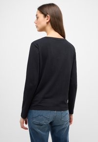 Schwarzes Langarmshirt mit rundem Ausschnitt, aus weichem Stoff. Verfügt über eine lockere Passform und flache Nähte, kombiniert mit blauen Jeans.
