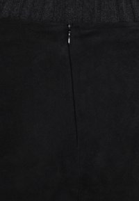 Svart mockaskorts med en texturerad midja och en central dragkedja bak för enkel påtagning. Slät, matt yta genom hela skäret.