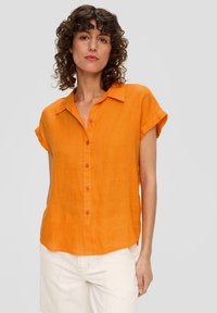 Camicia di lino arancione a maniche corte con colletto, dotata di una chiusura frontale con bottoni e un orlo rilassato, leggermente curvato.