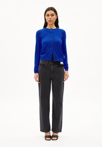 Blauer langärmliger Cardigan mit Rundhalsausschnitt und Knopfleiste, kombiniert mit schwarzen High-Waist-Jeans und schwarzen Slipper-Sandalen.