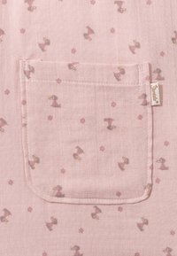 Pink fabric featuring a repeated pattern of small ducks in dresses and pink flowers. Includes a top pocket with rounded edges.