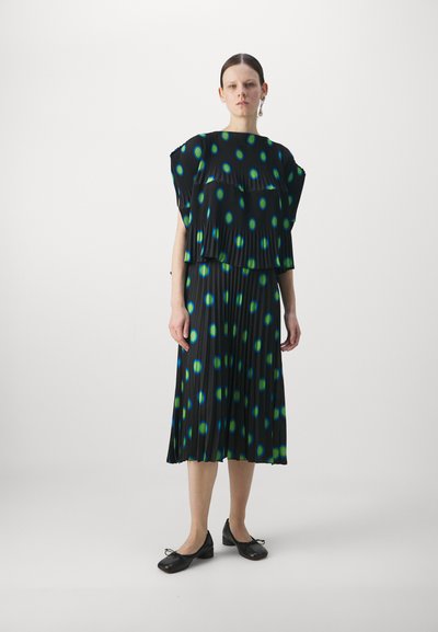 Black pleated dress with layered design, featuring green and blue polka dot patterns. Accompanied by black flat shoes.
