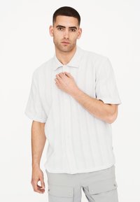 Camisa de manga corta, abotonada, en gris claro con un patrón de punto texturizado y rayas verticales. Con cuello y mangas enrolladas.