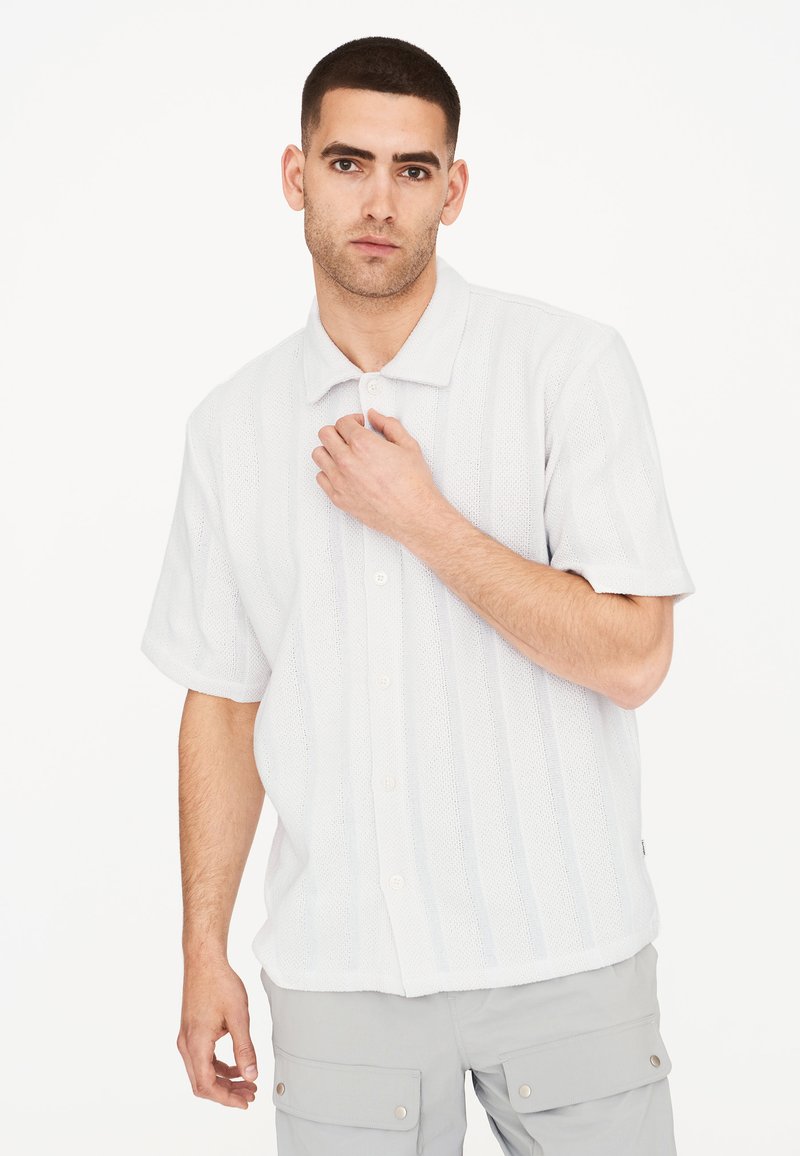 Camisa de manga corta, abotonada, en gris claro con un patrón de punto texturizado y rayas verticales. Con cuello y mangas enrolladas.