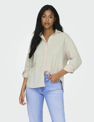 Lys beige button-up skjorte lavet af et tekstureret stof, med opslået ærmer og en afslappet pasform, parret med lyseblå jeans.