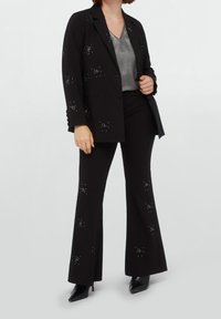 Black suit with flared pants and a fitted blazer. Embellished with silver studs, layered over a grey satin top. Smooth fabric texture.