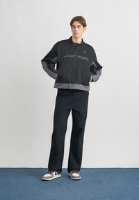 Black and gray jacket with a high collar and zip closure. Features "Jordan" logo on front. Paired with black pants and sneakers.