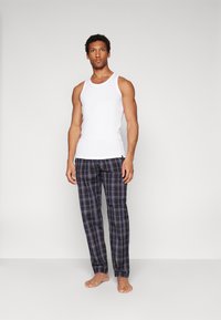 Top alb cu bretele și pantaloni de pijama în carouri bleumarin cu accente în gri deschis și mov, fabricați dintr-un material moale, având talie elastică.