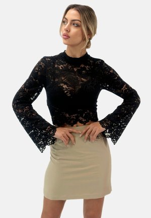 Haut en dentelle noire avec de longues manches cloche ; design court ; présente des motifs floraux. Associé à une mini-jupe beige clair. Texture lisse.