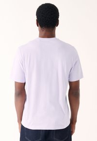 Vaaleanvioletti lyhythihainen t-paita, valmistettu pehmeästä kankaasta. Siinä on tavallinen pyöreä kaula-aukko ja rento istuvuus, ilman näkyviä kuvia tai kuvioita.