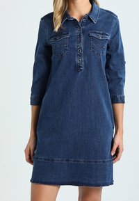 Vestido de mezclilla con cuello, parte delantera con botones, dos bolsillos en el pecho, mangas de tres cuartos y dobladillo deshilachado. Color azul oscuro.