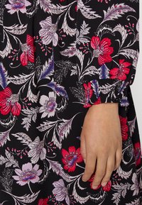 Černá látka s živým květinovým vzorem v červené, fialové a bílé barvě. Rukáv má nařasený elastický detail, který zvyšuje atraktivitu designu.