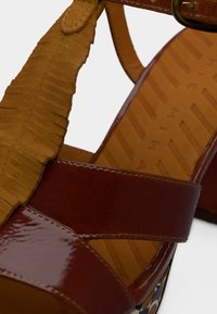 Καφέ δερμάτινο σανδάλι με λουρί καφέ με φουντίτσες, ανοιχτό δάχτυλο και δομημένη σόλα. Διαθέτει αγκράφα και μαξιλαρωμένη εσωτερική σόλα.