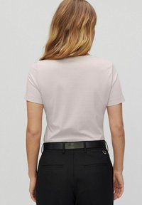 Lichtroze t-shirt met korte mouwen en een ronde hals, gecombineerd met zwarte broeken en een zwarte riem, gezien vanaf de achterkant. Zachte textuur.